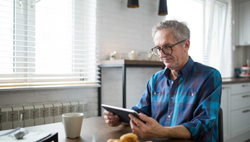 Oudere man op tablet aan keukentafel